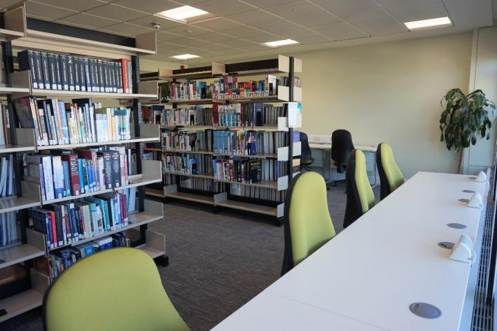 A photograph of desks inside the Western General Library, with book shelves behind the desks in the background.