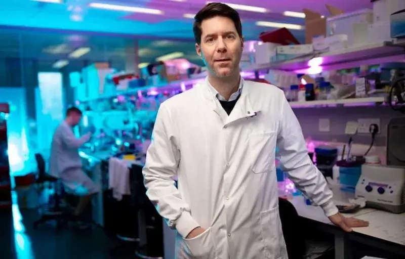 Professor Steve Pollard wearing a white lab coat, standing in the lab