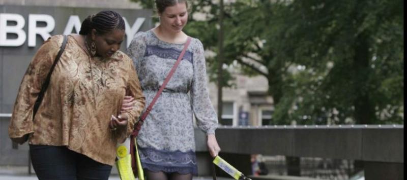 Blind student with guide dog and helper outside the University library