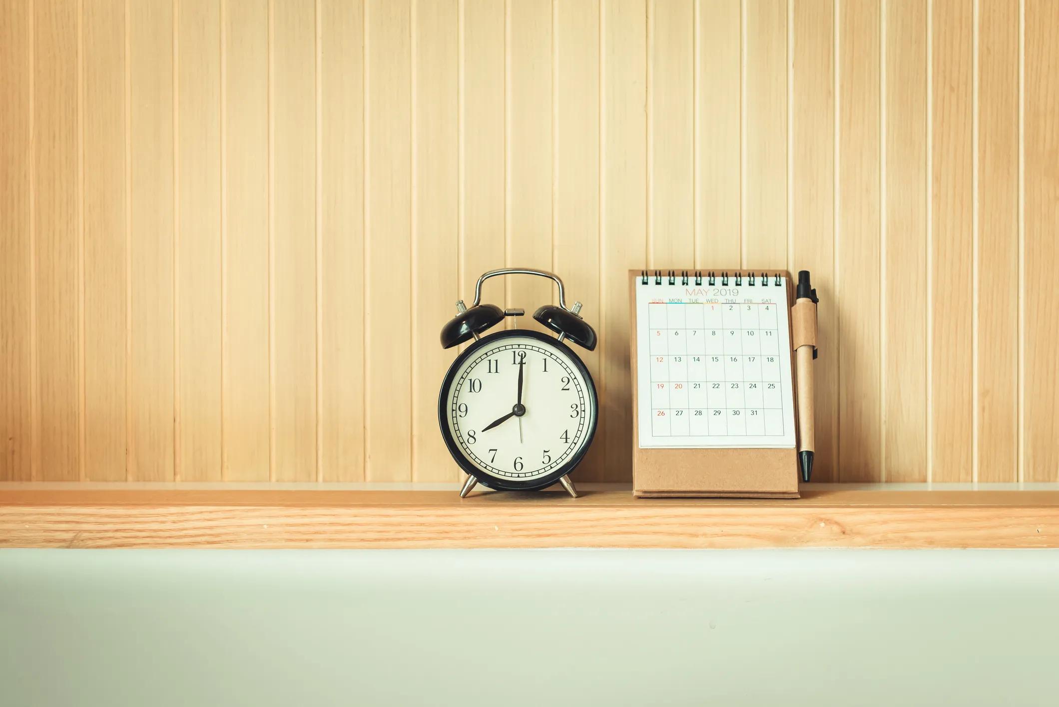 Image of an analogue alarm clock and calendar on a shelf