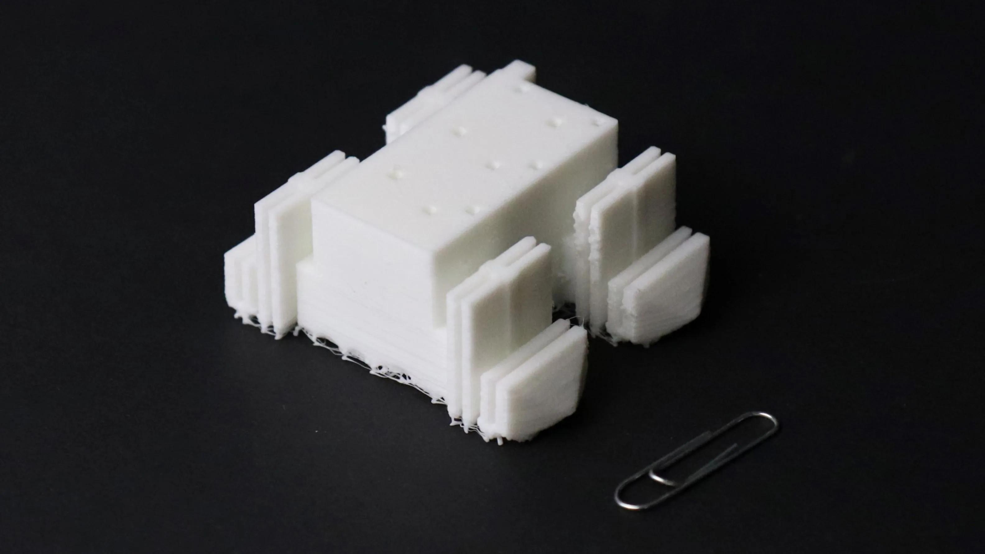 A four-legged robot made of soft plastic next to a paperclip