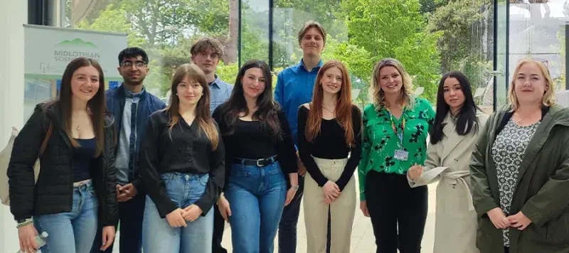 Group of people standing in front of windows looking out on trees