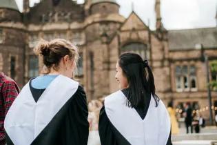 Two students in graduation gowns with their backs to the camera.