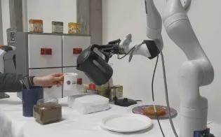 Coffee-making robot pours water from a kettle into a cup held by a person
