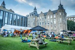 People sit at benches and seating outside at the Edinburgh International Book Festival, held at Edinburgh Futures Institute in 2024