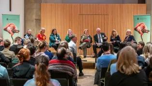 Photo taken of the behind an audience of school pupils at a hustings event. The stage has seven councillors from across Edinburgh, alongside Professor Jen Ross who chaired the hustings.