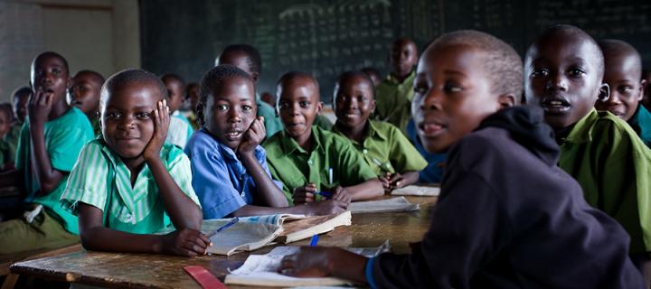 Photo of children in classroom, sitting at desks and smiling for camera