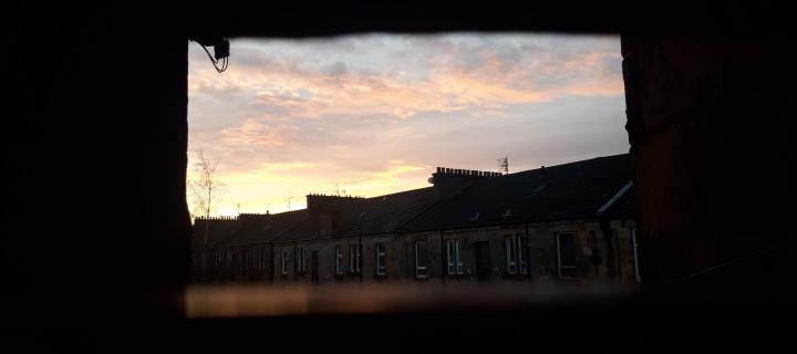 A photograph of the sky in winter, just after sunset. Tenement flats are silouhetted against pink clouds.