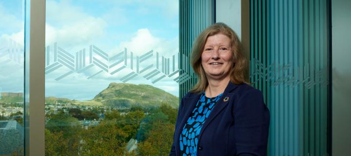 Dr Lorraine Kerr standing in front of a large window with panoramic view of Edinburgh behind her