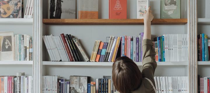 person reaching for a book on a bookshelf