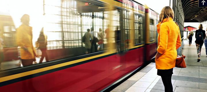 Woman in yellow coat standing on the platform of a railway station as a train arrives or departs