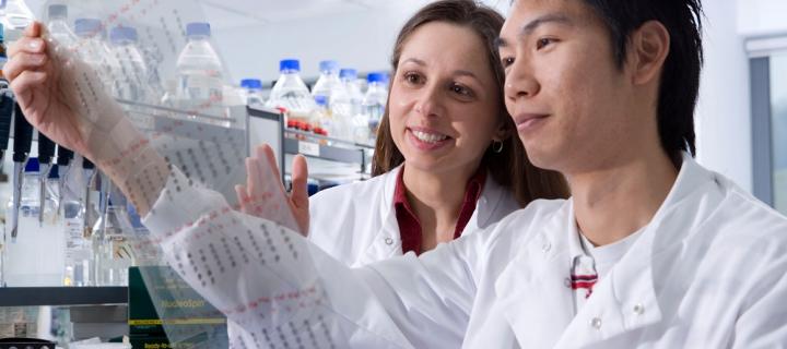 2 students in white lab coats examining experimental results in a research lab