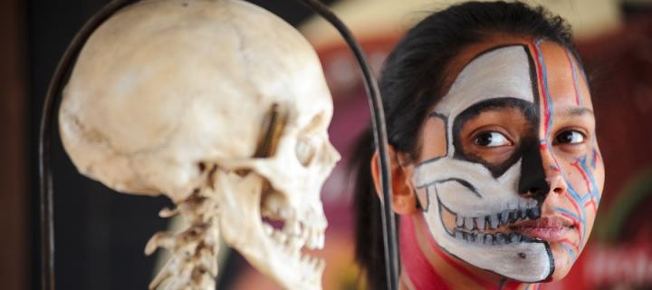 A girl with her face painted with the image of a skull next to a skull