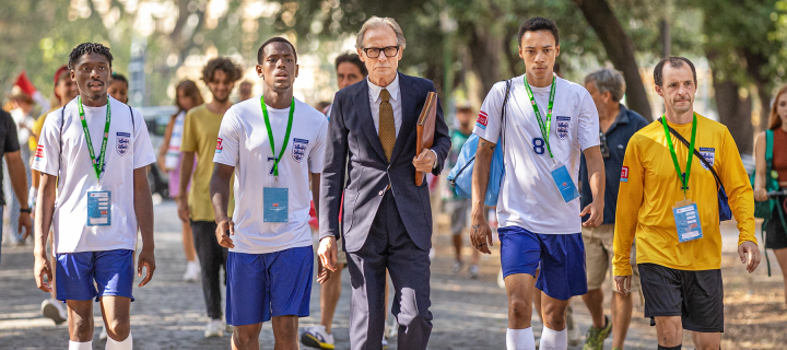 'The Beautiful Game' coach and player characters walking down a street wearing sports uniforms.