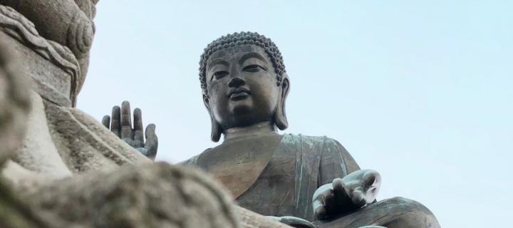 Looking up at a statue of the seated Buddha against a blue sky