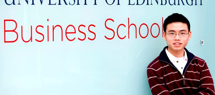 A student standing in front of a wall with the University of Edinburgh Business School sign 