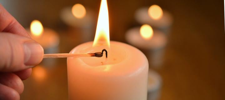 Photograph of a white candle being lit by a match. 