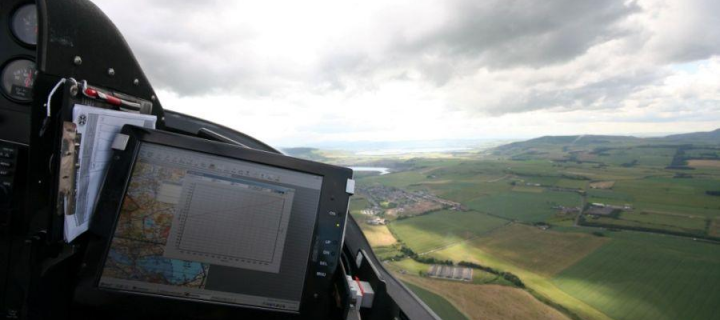 View from an airplane cockpit in flight overlooking green mountains, with a cockpit instrument panel in the shot