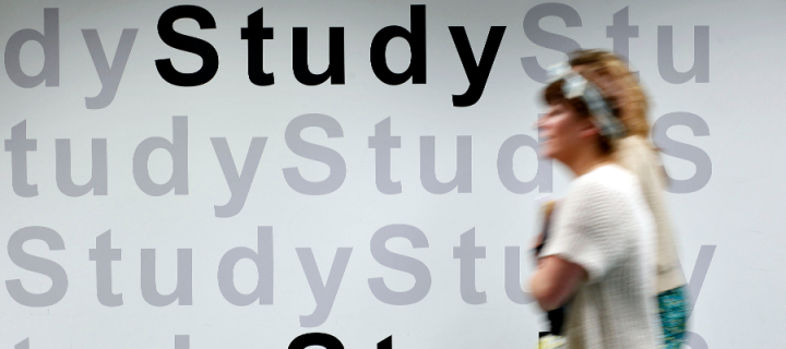 A female student walking past a wall with painted words that say 'study'
