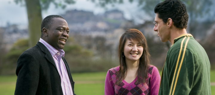 Two men and a woman standing in a park and talking