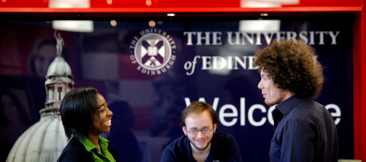 A woman and two men smiling and talking in front of a University of Edinburgh welcome sign