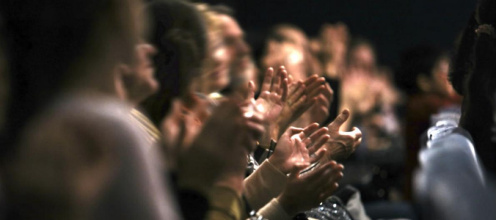Audience hands clapping in a dark auditorium