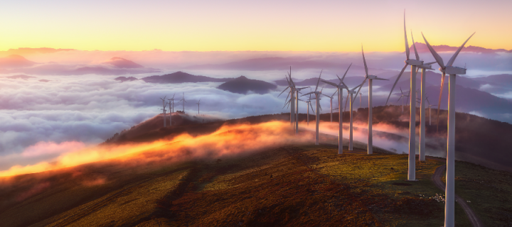 Wind turbines on a mountain at sunset, with clouds below the mountain peak