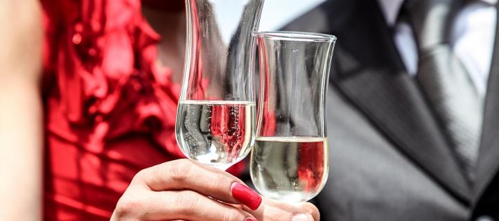Cropped image of young woman in red dress and man in suit both raising glasses to the caamera