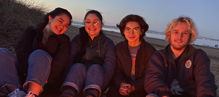 Image features four students sitting on Portobello beach smiling by the fire