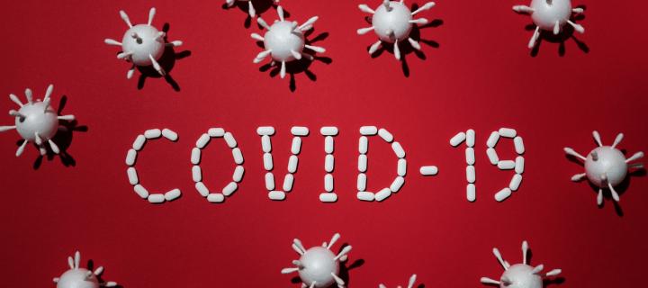 The word COVID-19 on a bright red background with corona viruses around the word. 