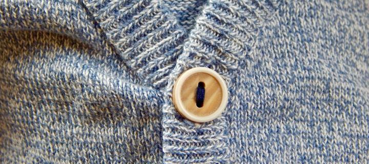 A close up photograph of a blue cardigan with a brown button.