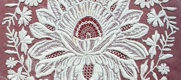 white embroidery of a flower on a white gauze background, mounted on red fabric