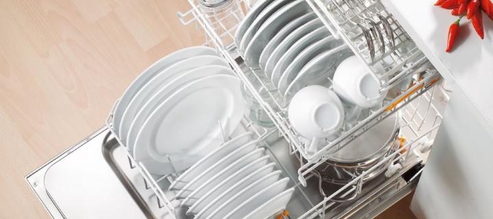 A photo of an open dishwasher. Inside the dishwasher is full of plates and cups.