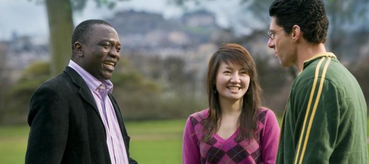 Colour photo of three students talking in a park. 