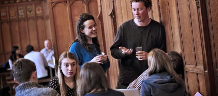 Colour photo of seven students talking inside the School of Divinity's Rainy Hall. 