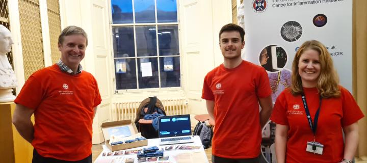 3 people wearing red t-shirts, standing in front of a table with a card game school resource