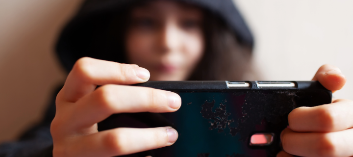 child with hood up looks at phone