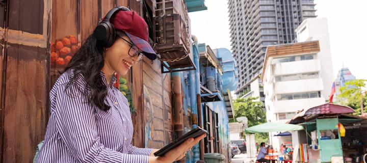 Student sits in a city street with headphones and tablet learning