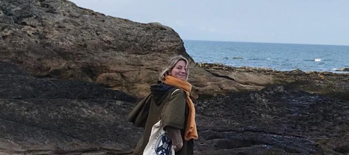 Photo of Elisabeth standing on the seashore looking directly at the camera