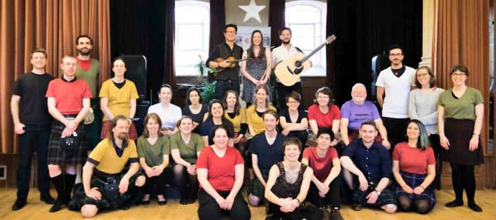 A group of ceilidh dancers in a local community hall, posing with the ceilidh band in the background.