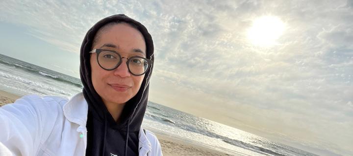 Head and shoulders photo of Francisca Da Silveira on a beach with her hood up