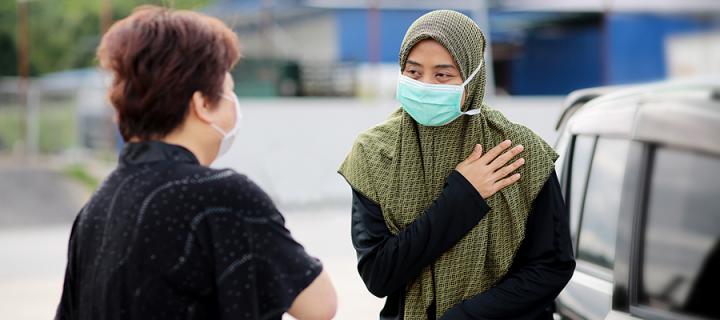 Two Malaysian individuals greet each other wearing face masks