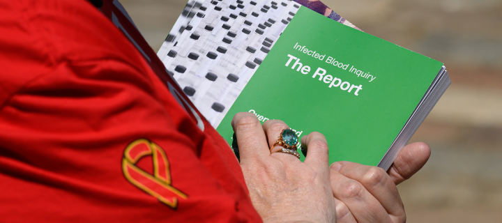 A person holds a report with the title 'Infected Blood Inquiry The Report'