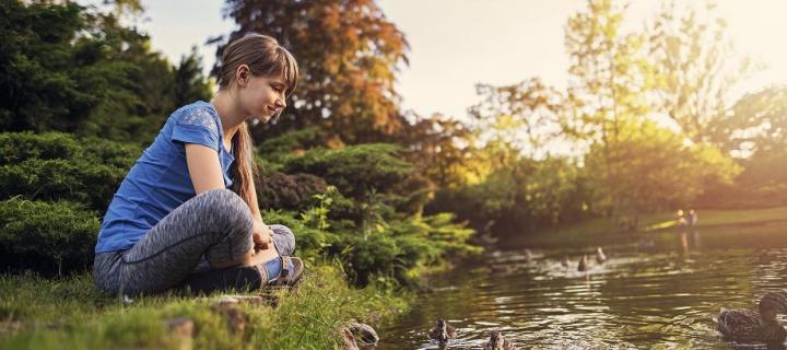 Photograph of a teenage girl sitting on a river bank looking at ducks