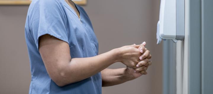 Woman in blue hospital scrubs, disinfecting her hands
