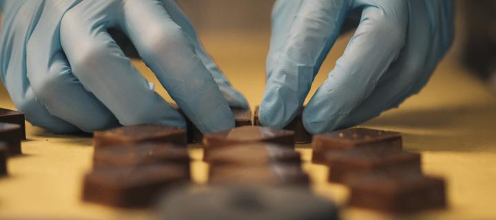 A close up photograph of chocolates being prepared for decoration by a pair of gloved hands