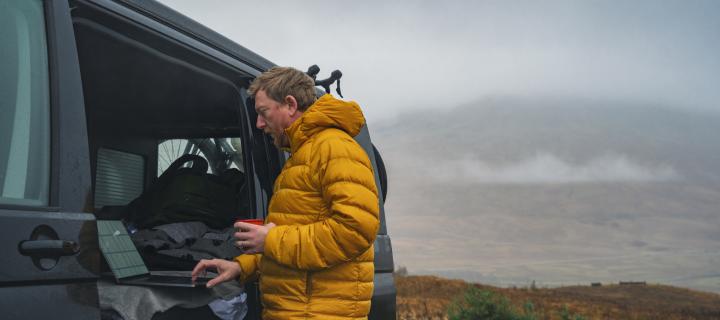 Mature man catches up with some work on his laptop whilst in his campervan in the Scottish Highlands