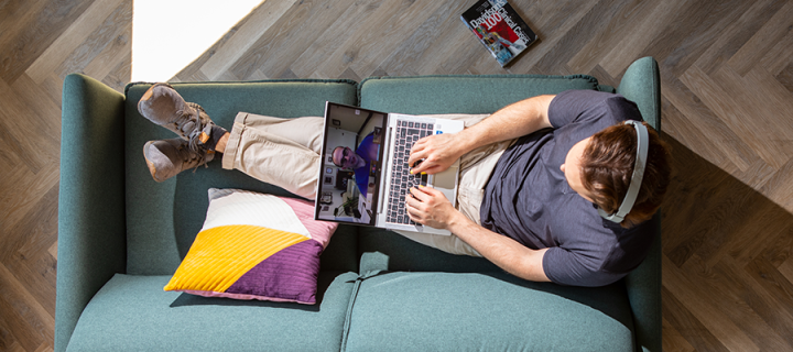 top down view of a person lounging on a sofa while working on a laptop