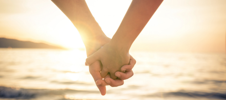 Couple holding hands on beach with sea in the background