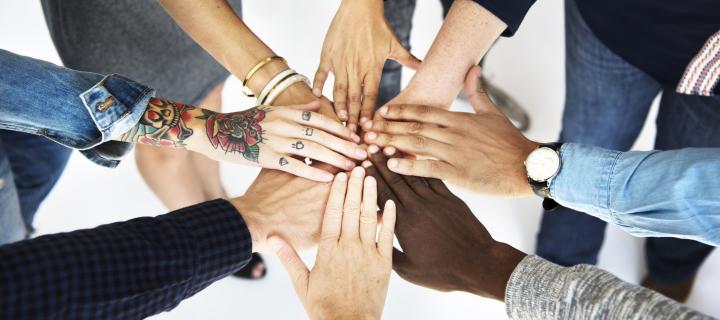 Photo of eight hands of different colours clasping each other supportively